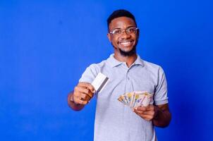 happy and excited young african man holding bundles of cash and card photo