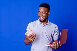 young african businessman holding a lot of money and using his laptop photo