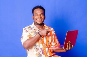 Portrait of young modern businessman standing holding laptop and looking at camera with happy smile photo