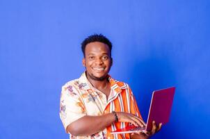 Portrait of young modern businessman standing holding laptop and looking at camera with happy smile photo