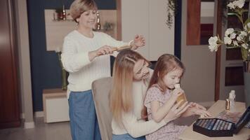 hija y mamá oler perfume. Tres generaciones de mujer de un contento familia. un abuela, un joven niña y un pequeño niña - nieta gastar hora abrazando, sonriente, riendo en frente de el espejo video