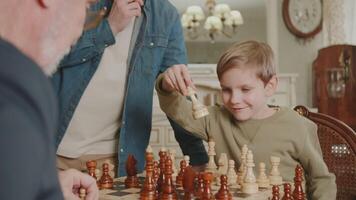 de kind herschikt de schaak stuk Aan de schaakbord. vader is gelukkig voor zijn zoon, wie, spelen schaken, schaakmat zijn opa. vaderlijk steun. een familie hobby. video