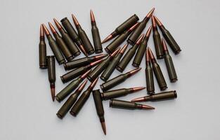 Unitary cartridges with copper alloy shell bullets for assault rifle scattered on a white surface top view photo