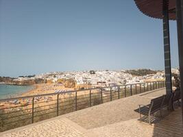 Scenic view of a coastal town with white buildings, beachfront, and clear skies, as seen from a shaded terrace. photo