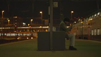Jeune homme avec noir frisé cheveux attendre solitaire à train station à nuit video