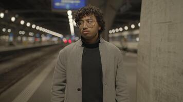 joven hombre con negro Rizado pelo esperando solitario a tren estación a noche video