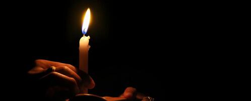 Hands holding a burning candle in the darkness background photo