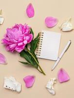 Peony flower and notepad on beige background. Holiday background. View from above. Copy space. photo