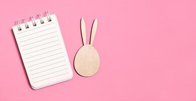 Easter background. Notebook and wooden rabbit on a pink background. Easter card. Copy space photo