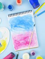 Painted notebook with a brush on a light blue background. Artistic objects for drawing. Flat lay. Copy space. photo