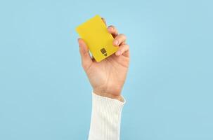 A female hand holds a yellow plastic bank card on a blue background. Bank concept. photo