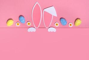 Easter background. Rabbit ears and Easter eggs on a pink background. Copy space. photo