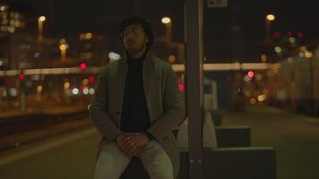 joven hombre con negro Rizado pelo esperando solitario a tren estación a noche video