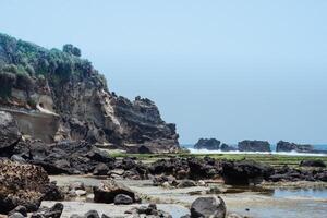 Beautiful beach view with white sand, rocks and calm waves under a bright blue sky. Summer vacation concept. Sayang Heulang Beach, Garut, West Java, Indonesia photo