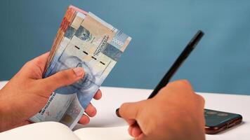 a man is writing on a notepad with banknotes in hand. the concept of income and expenditure finance photo