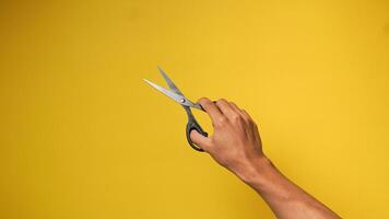 Man's hand holding black scissors on a yellow background photo