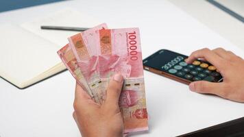 a man is counting Indonesian rupiah banknotes with a calculator. financial management concept photo