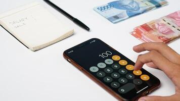 man's hand pressing a calculator and rupiah banknotes and notes on a white background photo