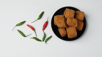 Fried tofu on a black plate with chilies in a white background photo