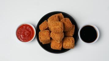 Fried tofu on a black plate with chili sauce and sweet soy sauce on a white background photo
