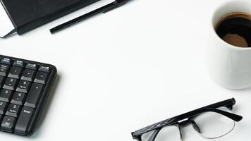 workspace desk with notebooks, pens, keyboard, glasses and coffee on white background photo