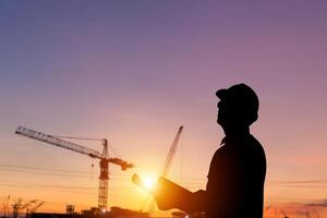 silueta de ingeniero hombre comprobación proyecto a edificio sitio, capataz trabajador a construcción sitio borroso puesta de sol en noche hora antecedentes foto