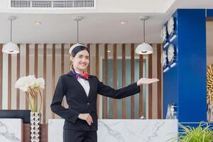 joven mujer recepcionista en pie y sonriente a el frente escritorio de el hotel recepción, retrato de hembra recepcionista trabajando en hotel foto