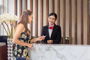 Focus on female travelers with bag travel luggage check-in at the hotel with blurred smiling female receptionist photo