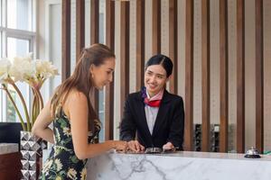 Focus on female travelers with bag travel luggage check-in at the hotel with blurred smiling female receptionist photo