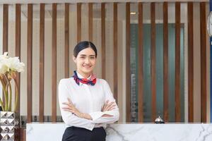 Young Asian woman receptionist at the hotel counter standing with arms crossed, Female receptionist working in the hostel photo