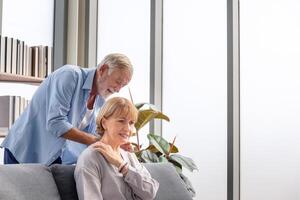 Senior couple in living room, Senior man with his wife at home, Woman with pain in the shoulder, Retired man taking care of wife, Family health care and support concepts photo