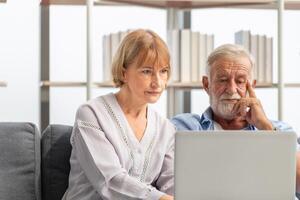 Senior couple using laptop checking their bills, retired elderly family reading documents photo