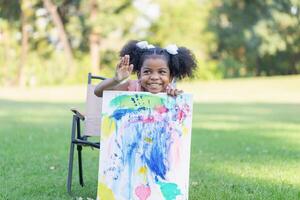 Cheerful little child girl shows her painting work. Cute kid show painting work in the garden photo