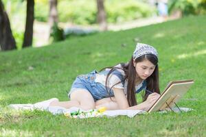 asiático Adolescente niña dibujo un imagen en el parque con caballete, paleta, y Cepillo de pintura foto