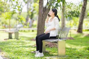 embarazada mujer sentado relajado en el parque y utilizando un teléfono inteligente foto