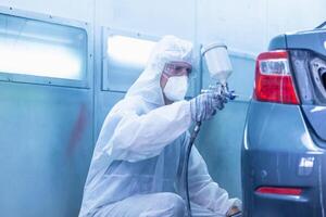 Mechanic painting car in the chamber. Worker using spray gun and airbrush and painting a car, Garage painting car service repair and maintenance photo