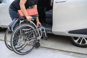 asiático invalidez mujer en silla de ruedas consiguiendo en su auto, accesibilidad concepto. foto