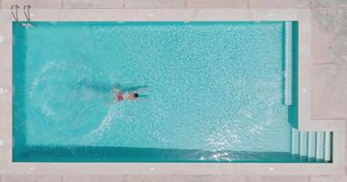 Top down view of a man in red shorts swims in the pool. Slow motion video