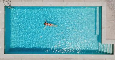 superiore giù Visualizza di un' donna nel rosso costume da bagno dire bugie su sua indietro nel il piscina. video