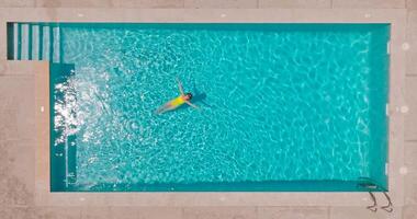 parte superior abajo ver de un mujer en amarillo traje de baño acostado en su espalda en el piscina. video