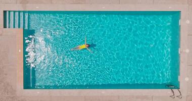 superiore giù Visualizza di un' donna nel giallo costume da bagno dire bugie su sua indietro nel il piscina. video