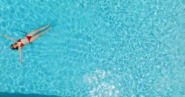 superiore giù Visualizza di un' donna nel rosso costume da bagno dire bugie su sua indietro nel il piscina. video