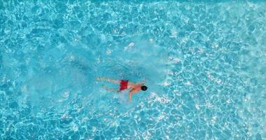 parte superior abajo ver de un hombre en rojo pantalones cortos nada en el piscina. lento movimiento video