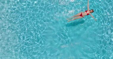 top naar beneden visie van een vrouw in rood zwempak aan het liegen Aan haar terug in de zwembad. video