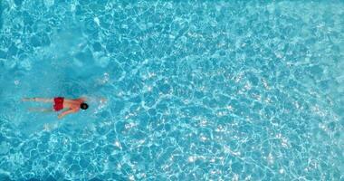 parte superior abajo ver de un hombre en rojo pantalones cortos nada en el piscina. lento movimiento video