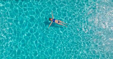 topo baixa Visão do uma mulher dentro azul roupa de banho deitado em dela costas dentro a piscina. video