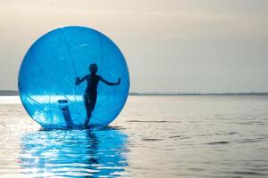 un niña en un inflable atracción en el formar de un pelota en el mar foto