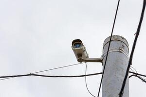 old CCTV surveillance camera on rusted pole at overcast day photo