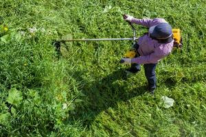 lawnmower man with string trimmer trimming grass at sunny day photo