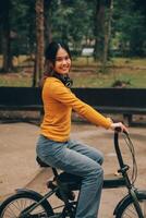 Happy young Asian woman while riding a bicycle in a city park. She smiled using the bicycle of transportation. Environmentally friendly concept. photo